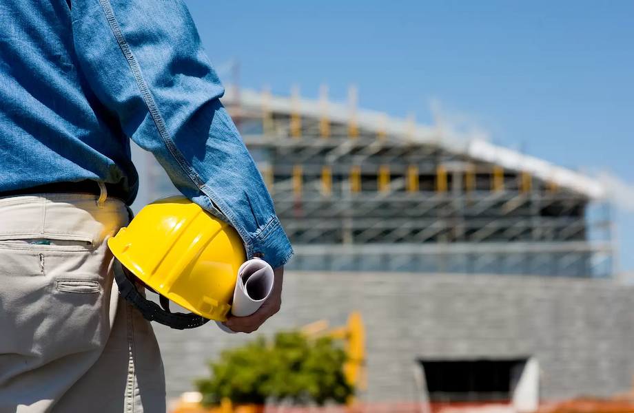 A man in blue jeans and a hard hat holding a yellow helmet, ready to do BREEAM assessments to improve building safety